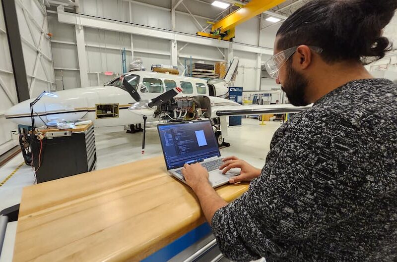 Technicien avec ordinateur devant avion en maintenance.